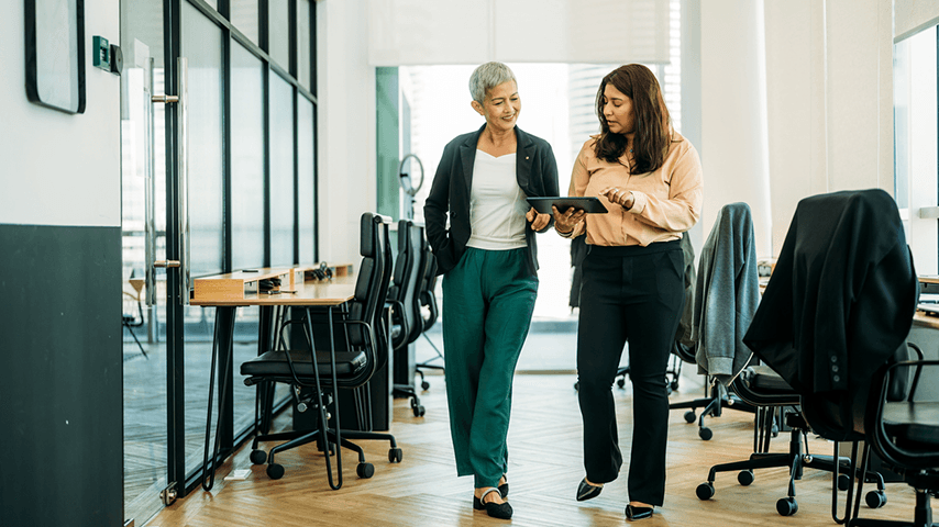 two women walking in office looking at tablet