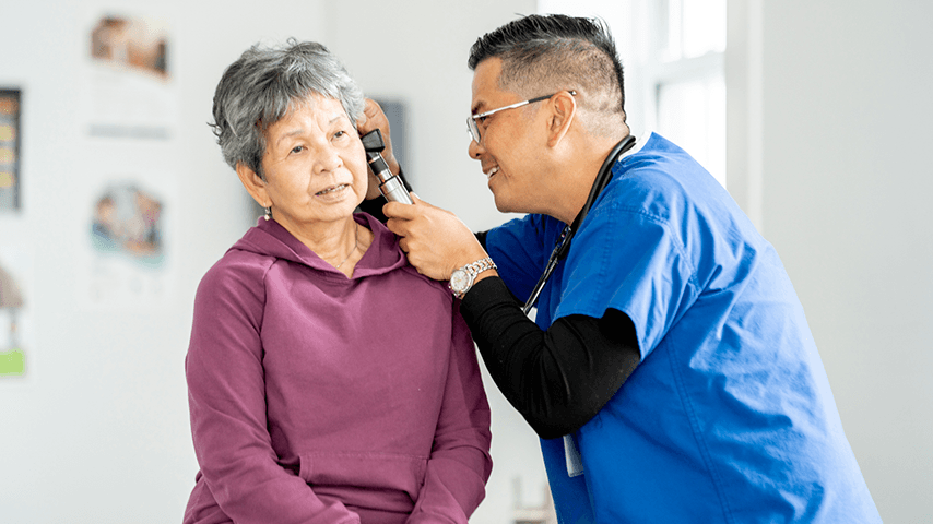 Asian male doctor examining older Asian woman's ear