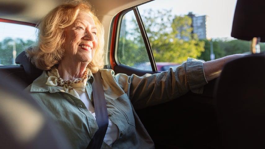 A white caucasian woman is sitting in the back of an Uber driver's car, enjoying a ride and happily looking out of her window.
