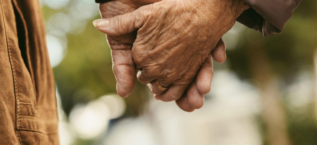 A closeup of a senior couple holding hands while walking outdoors.