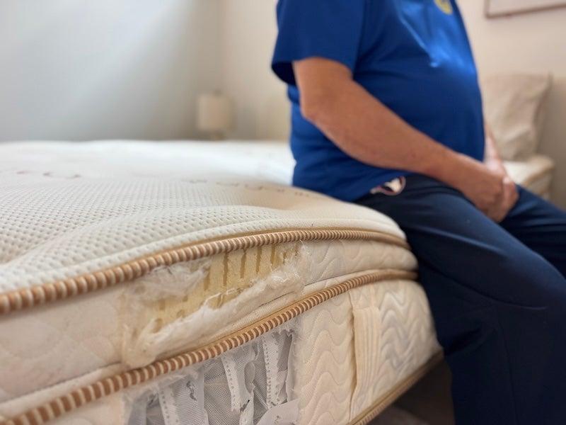 A man sits on the edge of the Saatva Latex mattress. An exposed cutaway shows the mattress’s internal layers of latex and coils