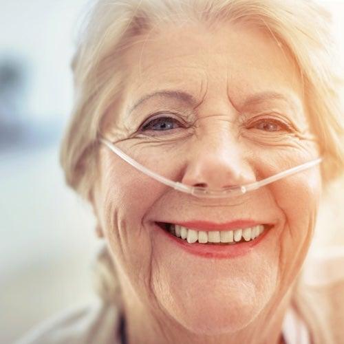 A woman with grey-blonde hair and an oxygen tube in her nose smiles at the camera