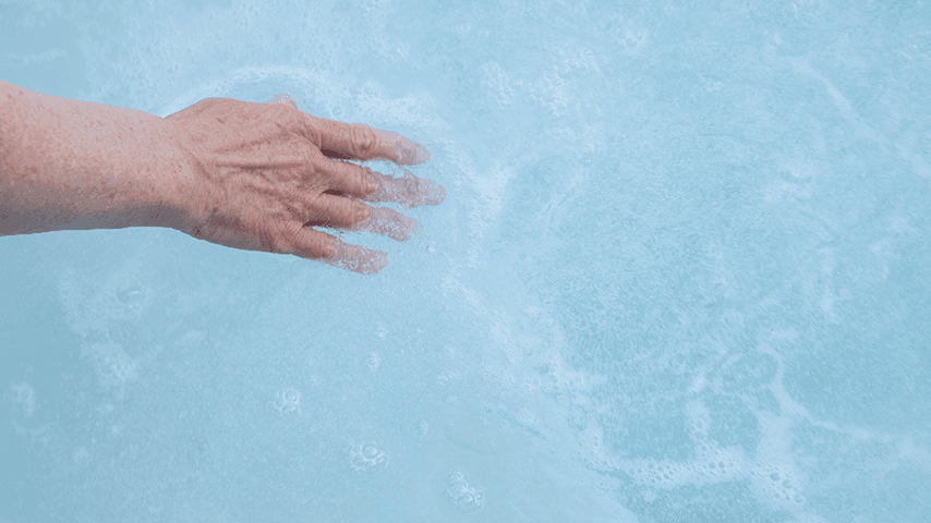 older woman's hand in bathtub water