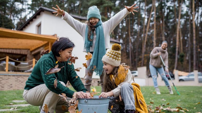 grandmother playing outside with granddaughters, mom raking leaves in the background