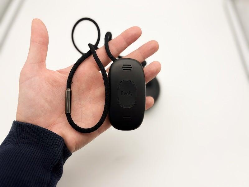 A hand holding the Lively Mobile2 medical alert device and necklace against a white background