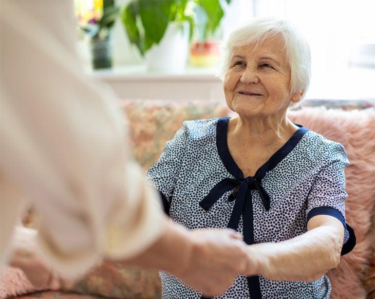 A senior Caucasian woman is receiving help getting up from a seated position from her caregiver.