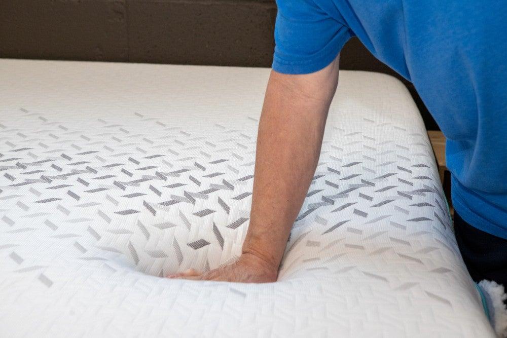 An older adult man pressing down on the plush top of the Nectar Premier Hybrid