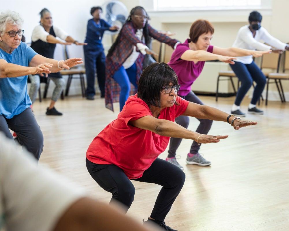 A group of older adults performing squats in a fitness class, focusing on balance and strength exercises.