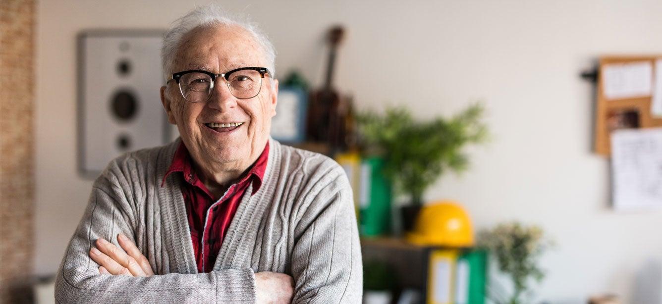 A senior man with glasses on is smiling while crossing his arms.