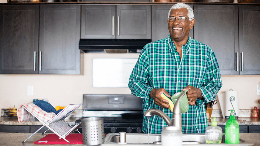 smiling black man in glasses washing dishes at sink