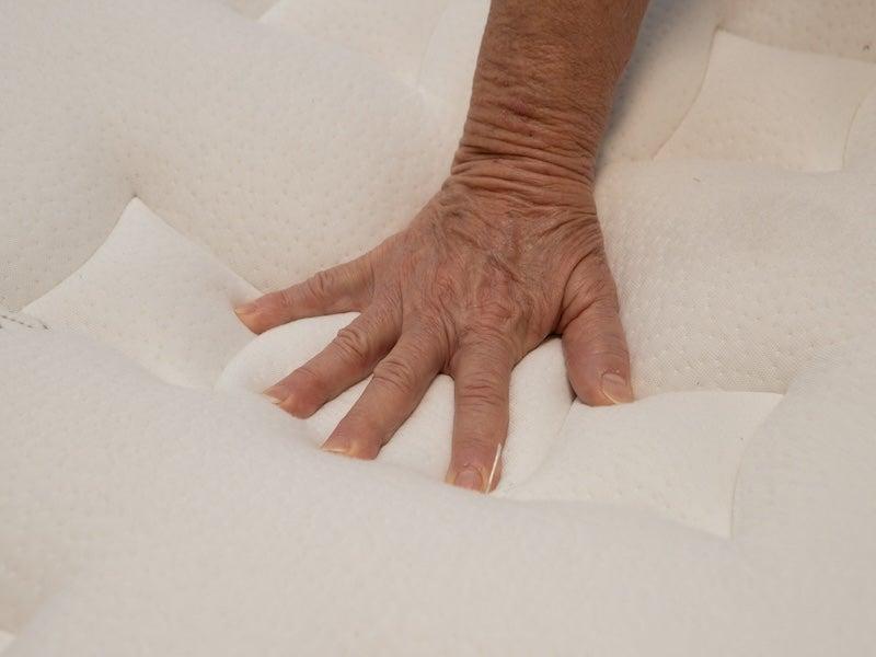 A hand presses down the top of the Nolah Evolution mattress.