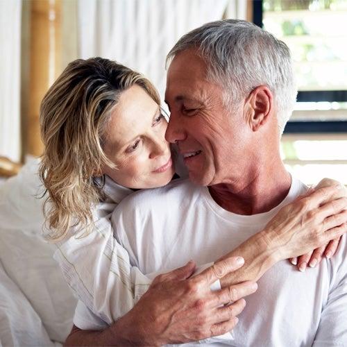 Man and woman smile and hug each other while in bed