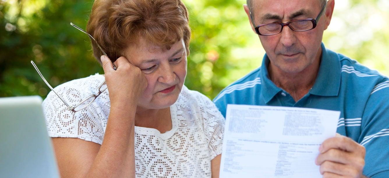 A senior Caucasian couple is sitting at a table discussing their Medicare plan, looking confused.