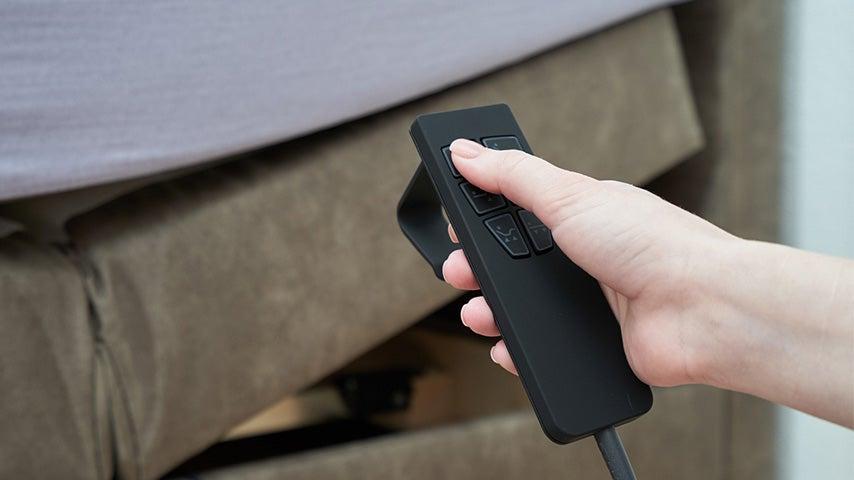 Woman pushes a button on her adjustable bed remote while the upper part of her bed rises upward
