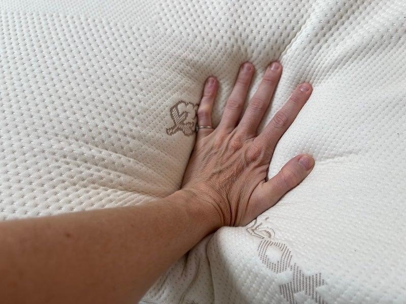 A hand presses down on a Saatva topper.