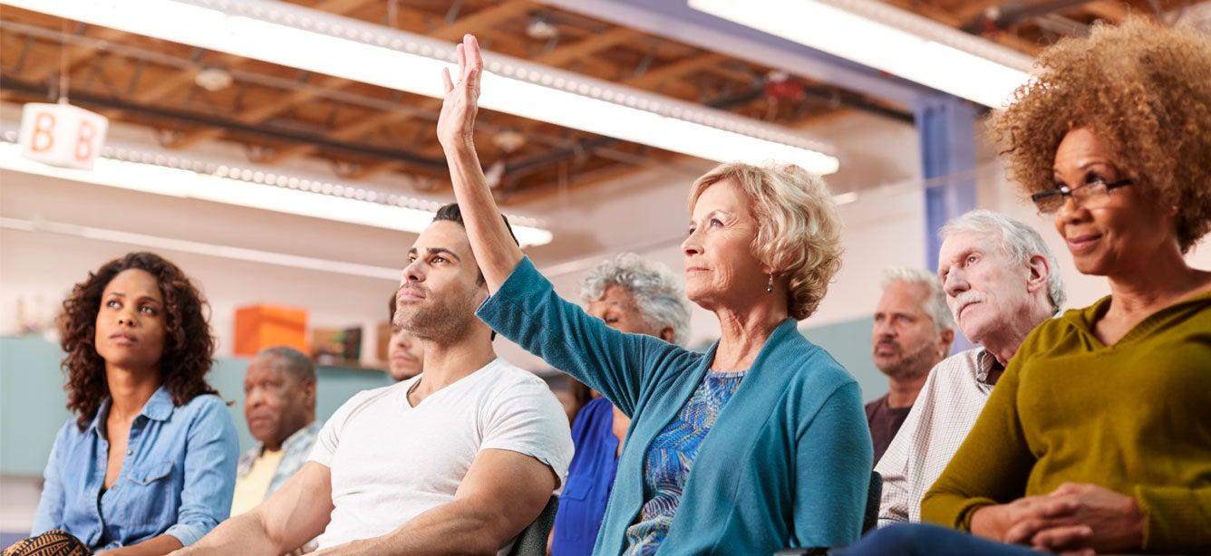 A woman raises her hand to ask at question at a community townhall with her member of Congress.