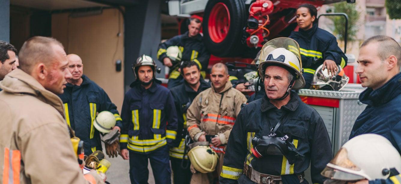 A fire chief is talking to his crew in front of a fire truck.