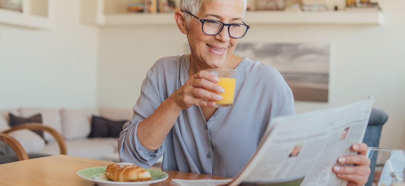 A smiling older woman with short, silver hair is enjoying breakfast.