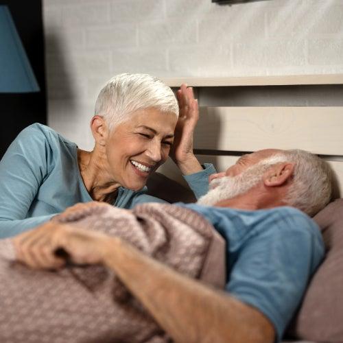 A man and woman laughing and talking while lying in bed